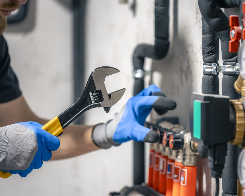 A man installs a heating system in a house and checks the pipes with a wrench. Adjusting heating valves in a residential building. A plumbing and heating technician works.