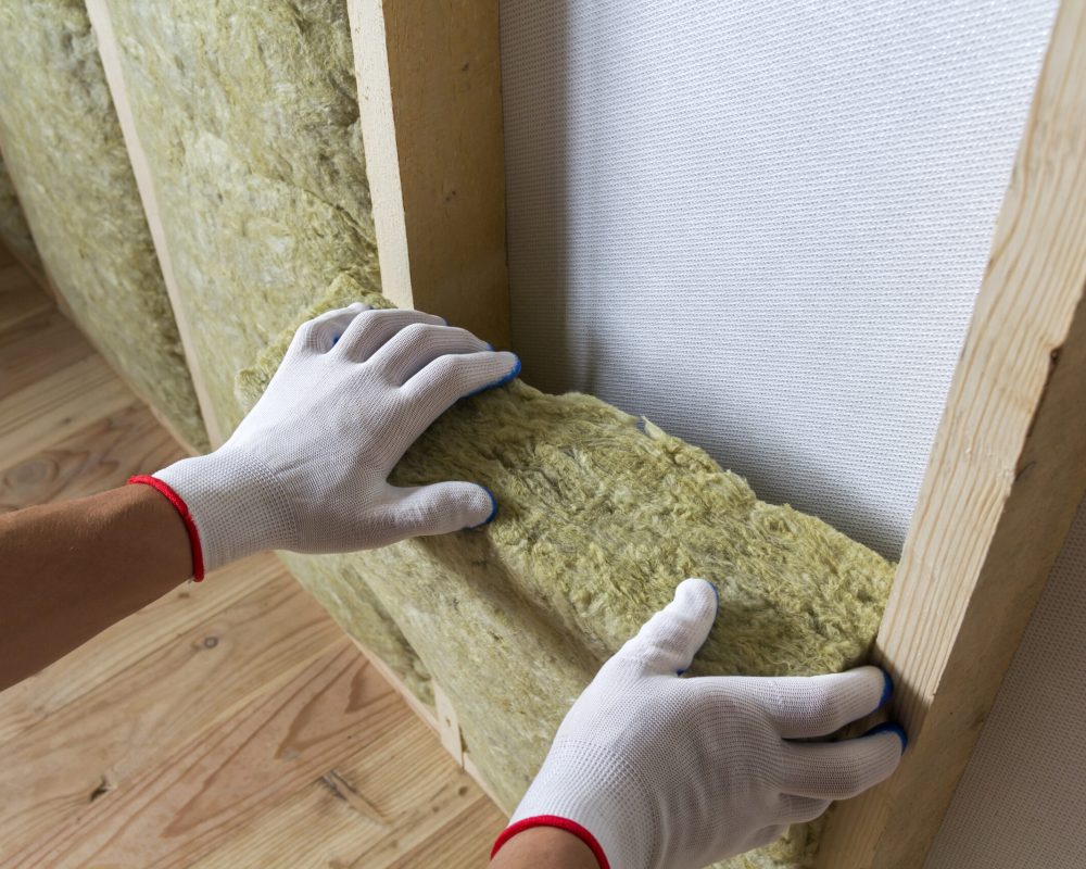 Close-up of worker hands in white gloves insulating rock wool insulation staff in wooden frame for future walls for cold barrier. Comfortable warm home, economy, construction and renovation concept.